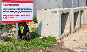 Seorang flag man memasang spanduk berisi keluhan terkait gaji dan nasib pekerja pengatur lalu lintas di tepi jalan dekat pintu masuk area Pertamina.