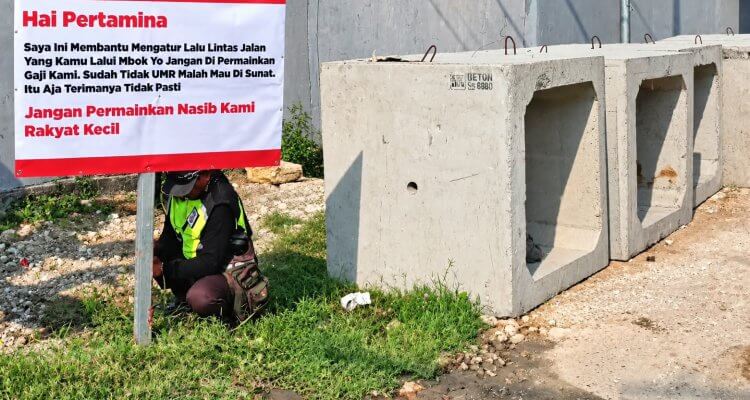 Seorang flag man memasang spanduk berisi keluhan terkait gaji dan nasib pekerja pengatur lalu lintas di tepi jalan dekat pintu masuk area Pertamina.